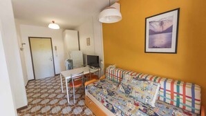 A compact living space with a sofa, a dining table with chairs, a television, and a framed picture on the wall. - Holiday apartment mit Klimaanlage (Bibione)