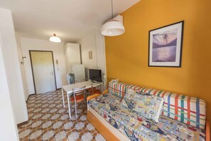 A compact living space with a sofa, a dining table with chairs, a television, and a framed picture on the wall. - Holiday apartment mit Klimaanlage (Bibione)