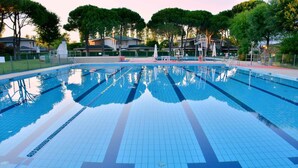 A swimming pool with clear water, surrounded by trees and a fence. - Holiday apartment mit Klimaanlage (Bibione)
