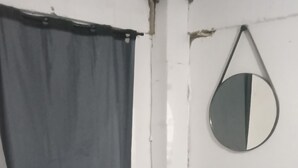 Huoneessa on punainen sohva, valkoinen seinä, harmaa verho ja pyöreä peili.