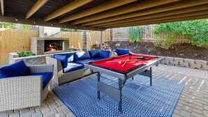 An outdoor patio with a pool table, blue cushioned seating, and a stone fireplace. - San Diego Family Getaway, 4BR Home Near Beaches & Balboa (Spring Valley)