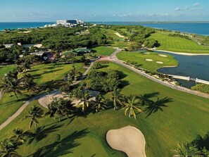 Eine Vogelperspektive eines Golfplatzes mit einem Wasserteil, Palmen und einem großen Gebäude im Hintergrund.