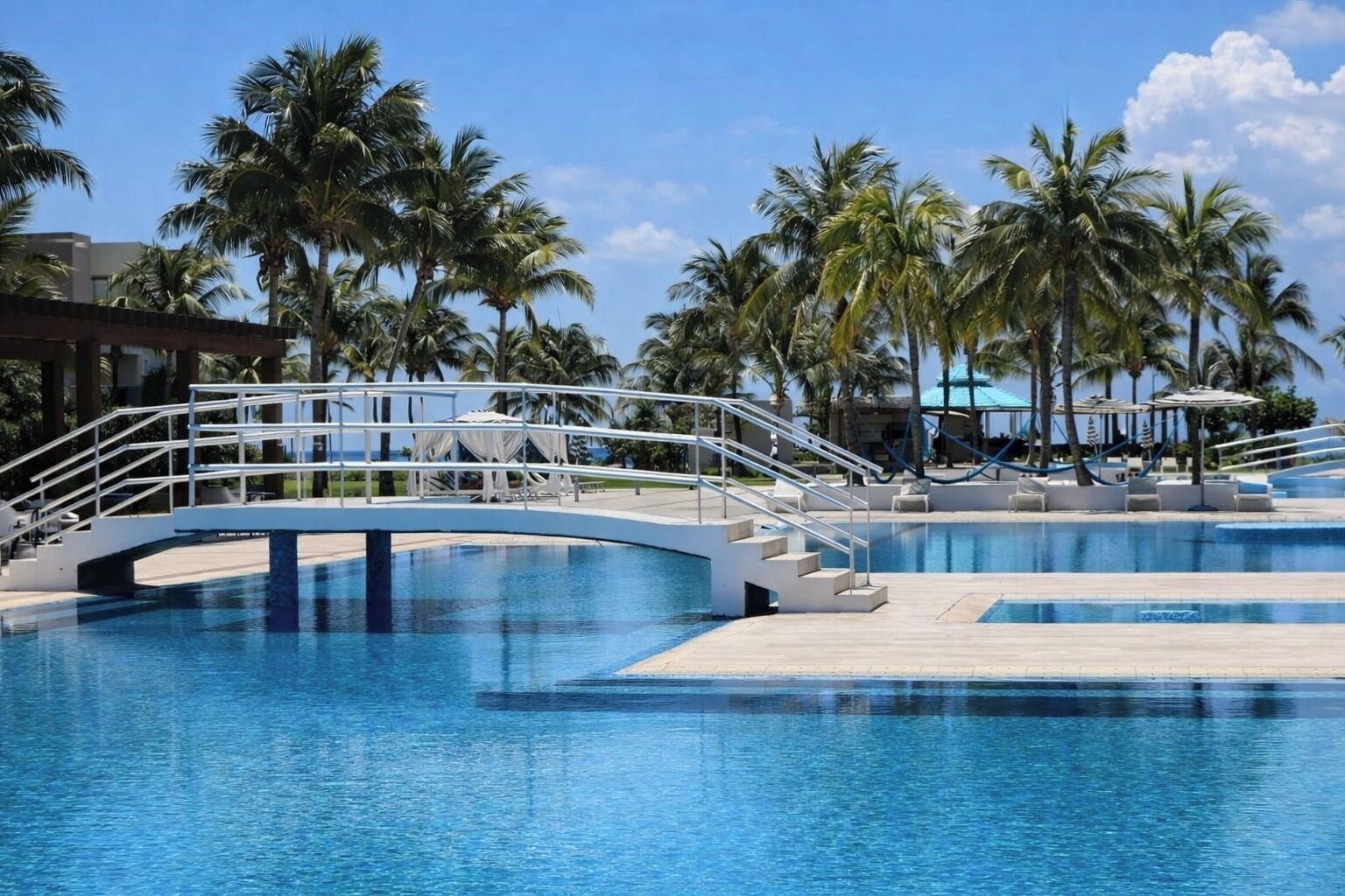A swimming pool with a bridge, palm trees, and a clear sky.