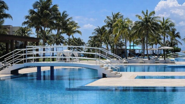 Una piscina amb un pont, palmeres i un cel serè.