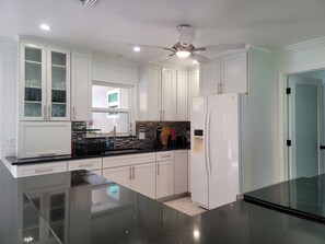 A kitchen with white cabinets, a black countertop, a white refrigerator, and a ceiling fan. - IMG Retreat • Heated Pool • 4BR (Bradenton)