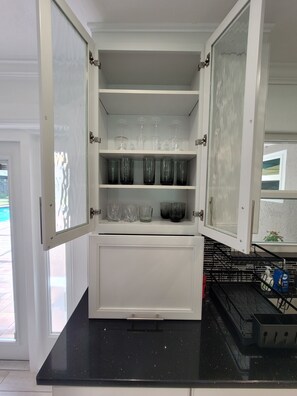 Una cocina con refrigerador empotrado, encimera negra y vitrina de vidrio con varios vasos.