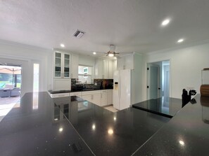 Una cocina moderna con armarios blancos, encimera negra y ventilador de techo.