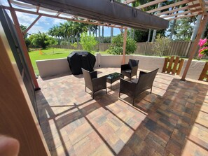 An outdoor patio with a grill, wicker furniture, and a view of a grassy yard. - IMG Retreat • Heated Pool • 4BR (Bradenton)