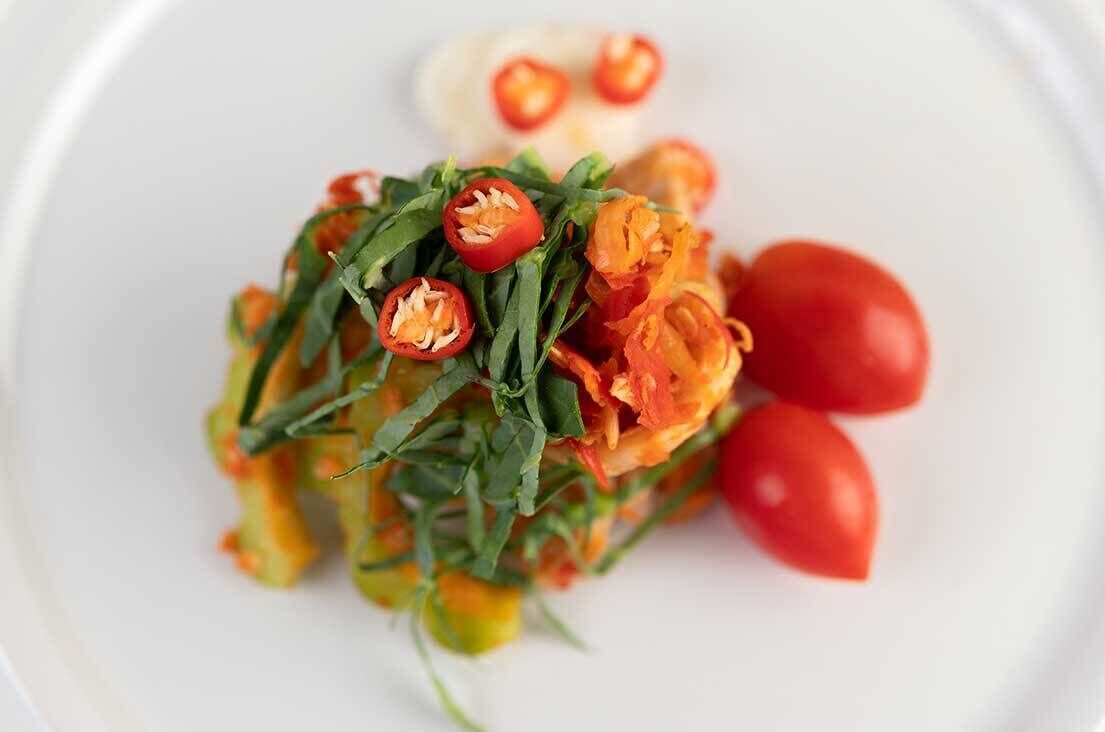 A white plate with a salad of greens, tomatoes, and red chili peppers.