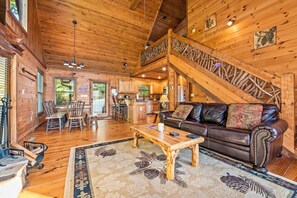 Interior de una cabaña de madera con comedor, sala de estar con sofá, una escalera y cocina.