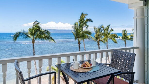 A balcony with a table and chairs overlooking the ocean, palm trees, and a clear sky. - Ocean view studio in vibrant West Maui for 2.-Lahaina Shores 511 (Lahaina)