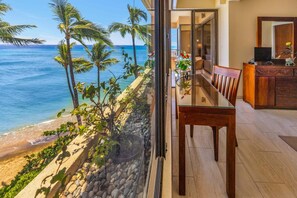 A dining area with a glass table and chairs, a view of the ocean, and a stone pathway leading to the beach. - Direct Oceanfront Corner 2BR with Panoramic Views -Sands of Kahana 243 (Lahaina)