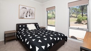 Une chambre à coucher comprenant un lit, une table de chevet, un ventilateur de plafond, une fenêtre avec vue et un tableau encadré au mur.