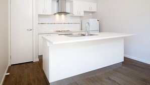 Une cuisine compacte avec des meubles blancs, une hotte en acier inoxydable, un évier encastré et un réfrigérateur blanc.