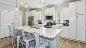 A modern kitchen with white cabinetry, a central island with bar stools, stainless steel appliances, and pendant lighting. - New Listing!| Lost Key| Dogs welcome| Two pools| Private Beach Club| Tennis| Free Golf (Pensacola)