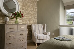 Une chambre avec une commode en bois, un fauteuil à rayures, un lit recouvert d’une couverture verte, une fenêtre donnant sur un paysage agréable et un radiateur.