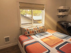 Un dormitorio con una cama, una ventana, un tendedero de pared y una rejilla de ventilación.