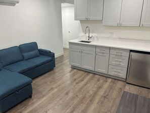 Una cocina moderna con un lavamanos empotrado, armarios blancos y un sofá azul.