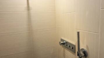 A shower with a handheld showerhead, a wall-mounted control panel, and a door handle.