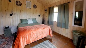 Een slaapkamer met houten lambrisering, een bed, een vloerkleed, een prullenbak en een raam met gordijnen.