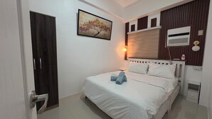 A hotel room with a bed, a door, a wall-mounted air conditioner, and a painting. - Cozy 1Bedroom Near Mactan Cebu International Airport (Lapu-Lapu)