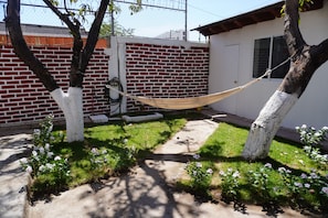 A backyard with a hammock, a brick wall, a white door, and flowering plants. - Hostal Mardan Puerto Vallarta Aeropuerto (Puerto Vallarta)