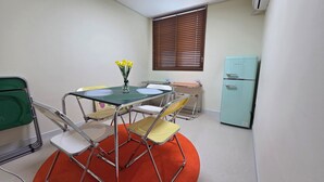 A compact room with a small table, four chairs, a refrigerator, and a window with blinds. - Hotel Dotori (Gunsan)
