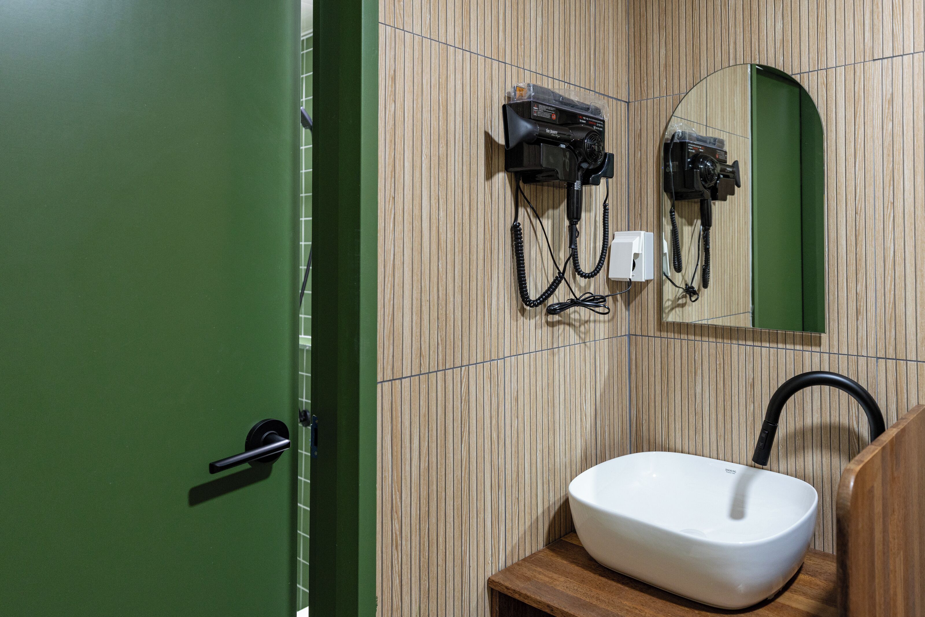 A bathroom with a green door, a white sink, a hairdryer, and a mirror.