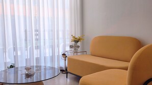 A modern living room with a sofa, a glass coffee table, and a side table with a clock and flowers. - Hotel Dotori (Gunsan)