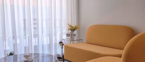 Una sala de estar moderna con un sofá, una mesa de centro de vidrio y una mesita auxiliar con un reloj y flores.