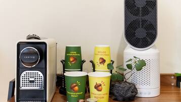 A coffee machine, two cups with 'Dormitory Hotel Dotori' branding, a speaker, and a small plant on a wooden surface.