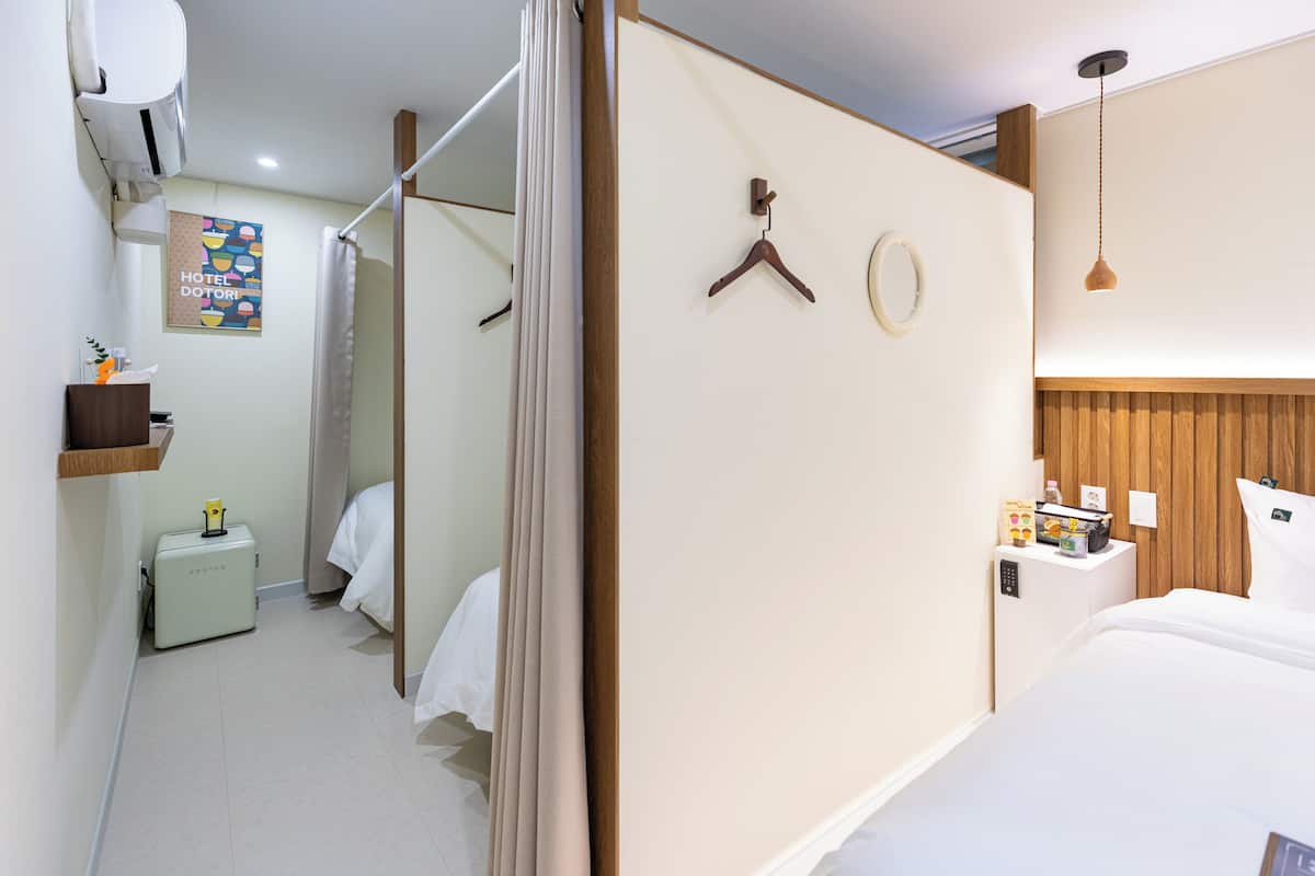 Habitación de hotel con cama, mesita de noche, lámpara colgante, armario, espejo y zona de ducha.