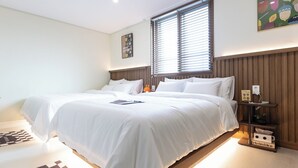 A bedroom with a large bed, a bedside table, a nightstand, a window with blinds, and a wall-mounted shelf with a sign. - Hotel Dotori (Gunsan)