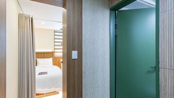 Habitació d'hotel amb llit, cortines, una porta verda i un interruptor a la paret.
