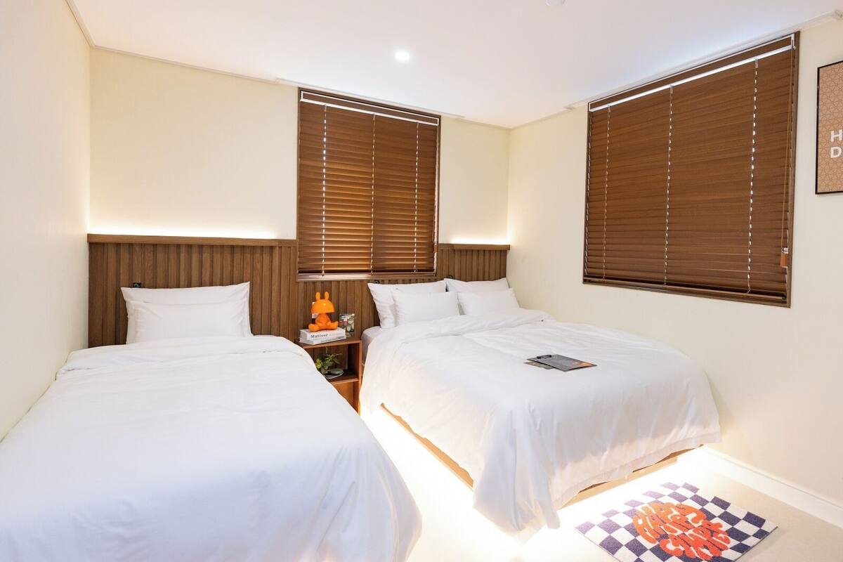 Habitación de hotel con dos camas, cabeceros de madera y una mesita de noche con una lámpara y una pequeña figurita naranja.