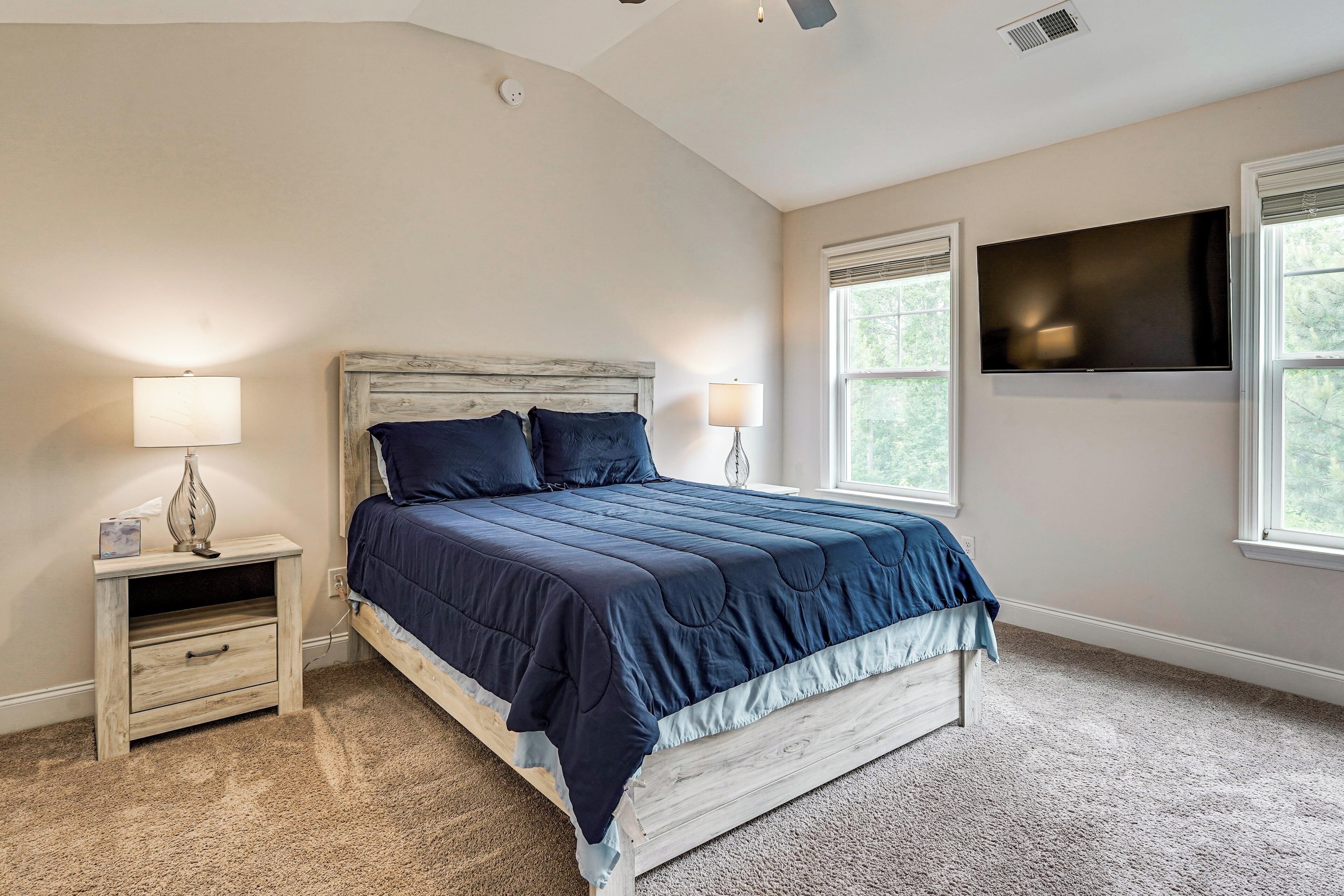 A bedroom with a bed, nightstands, a flat-screen TV, and windows.