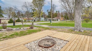 A deck with a fire pit, surrounded by a gravel area, with houses and a large tree in the background. - Walk to Silver Lake State Park! Family Getaway (Mears)