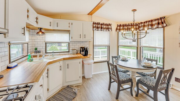 A kitchen with white cabinets, a wooden countertop, a gas stove, a sink, and a dining area with a table and chairs. - Walk to Silver Lake State Park! Family Getaway (Mears)