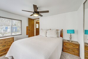 Un dormitorio con cama, mesitas de noche de madera, ventilador de techo y ventana con persianas.