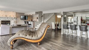 Een moderne woonkamer met een bank, een gestoffeerde fauteuil en een eethoek met barstoelen.
