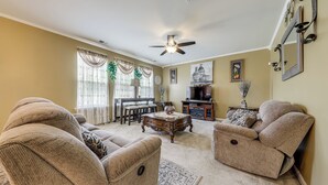 Ein Wohnzimmer mit zwei beigefarbenen Sofas, einem Couchtisch, einem Deckenventilator und einem Essbereich mit Tisch und Stühlen.