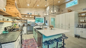 A modern kitchen with wooden ceiling beams, a central island with bar stools, and built-in white cabinets. - Blanco Riverfront Estate w/ 2 Homes: 4-Acre Oasis (Blanco)
