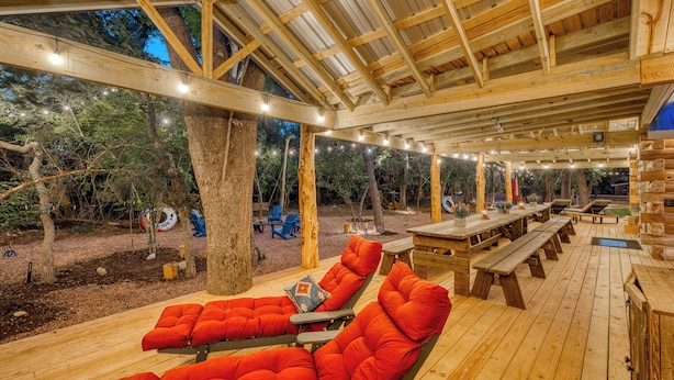 An outdoor wooden deck with benches and cushioned seating, surrounded by trees. - Blanco Riverfront Estate w/ 2 Homes: 4-Acre Oasis (Blanco)