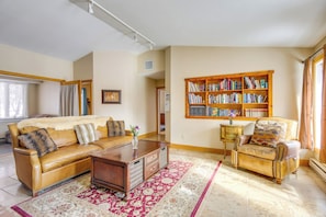 Een woonkamer met een leren bank, een houten bijzettafeltje, een tapijt met patroon, een boekenkast en een fauteuil met kussen.
