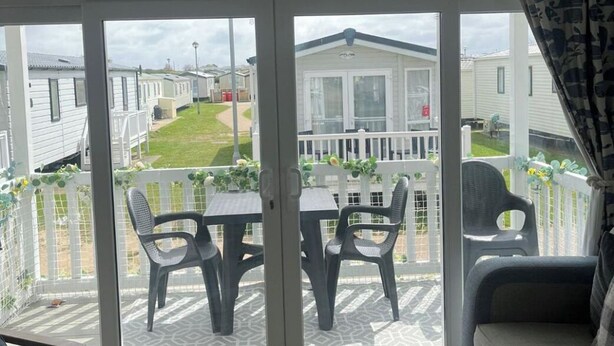 Un porche cubierto con una mesa y sillas, una cerca blanca y vistas a casas móviles.