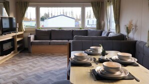 A modern living room with a sofa, a dining table set for four, a television, and a fireplace.