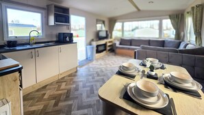 A modern kitchen with a microwave, sink, and window. There is a dining area with a table set for four, and a living room with a sofa and TV.