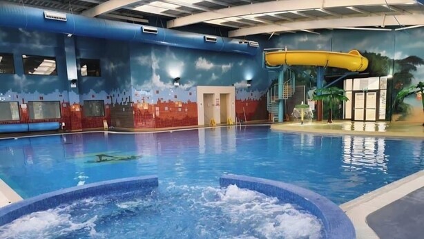 An indoor swimming pool with a water slide, a hot tub, and a mural depicting a city skyline.