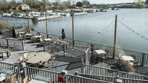 A waterfront restaurant deck with outdoor seating, a view of the marina, and a clear sky.