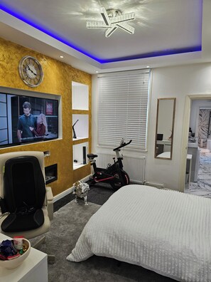 Una camera d'albergo moderna con un letto, una scrivania, una sedia, una TV, una bicicletta e una finestra con persiane.